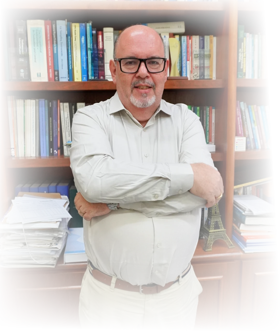Professor Antonio Carlos Vendrame de braços cruzados diante de sua estante de livros